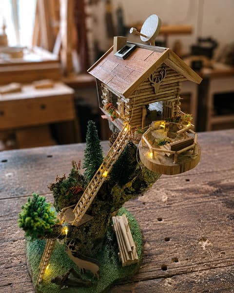 Beleuchtete Waldhütte aus Holz mit Balkon, Leiter, Moos und kleinen Waldtieren