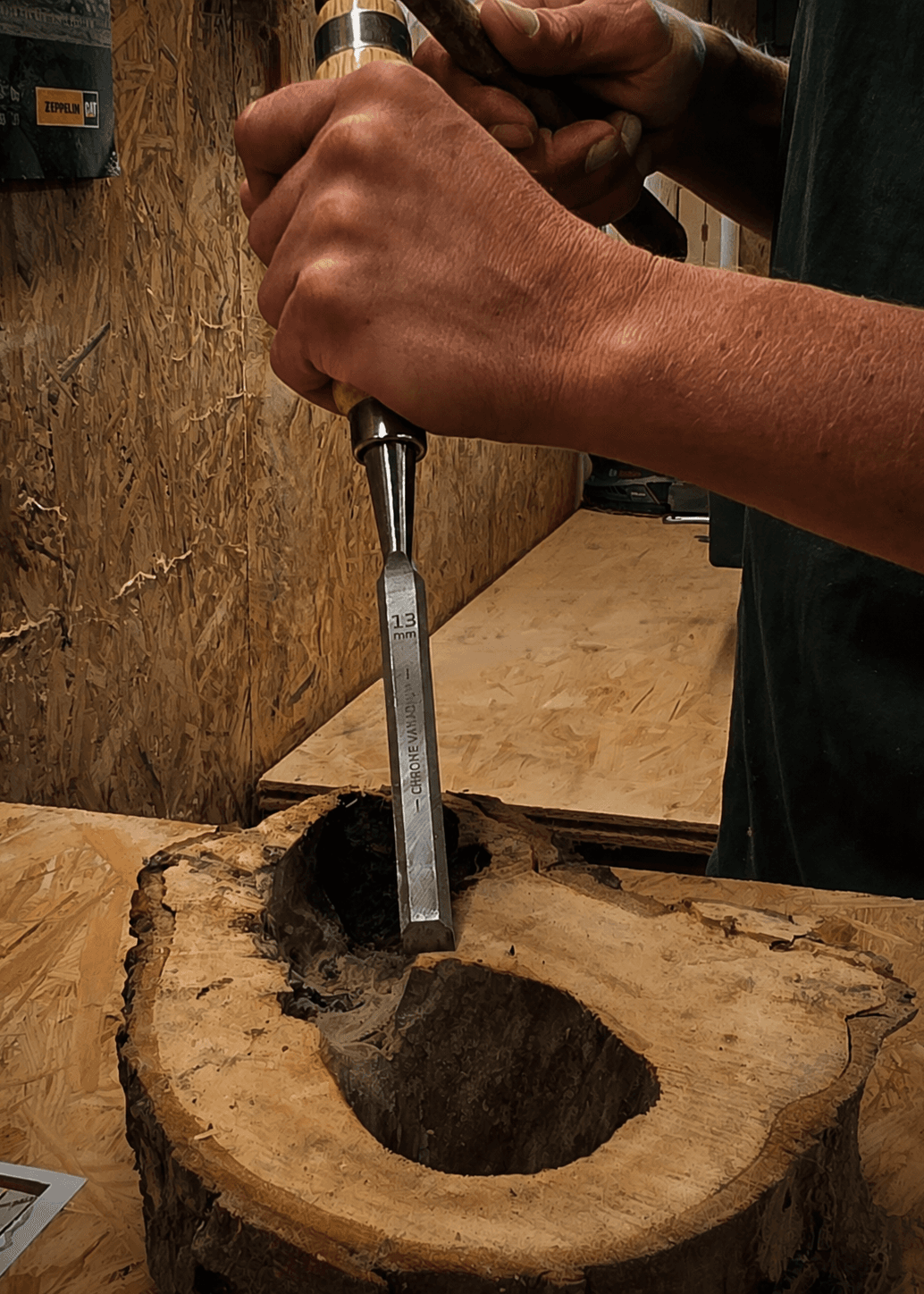 Hände schnitzen mit einem Stechbeitel eine runde Baumscheibe, umgeben von Holzspänen